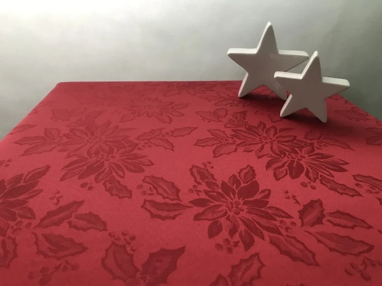 Czerwony obrus plamoodporny w gwiazdy betlejemskie i liście ostrokrzewu – widok na stole